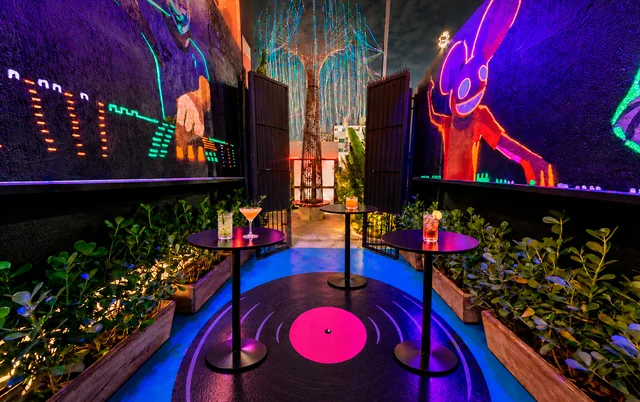 Mesas de apoio no fumódromo com piso em formato de disco e murais iluminados