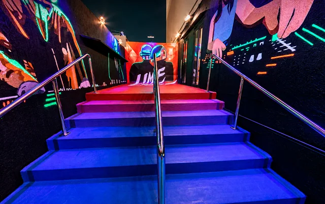 Escada do fumódromo com iluminação colorida e murais de músicos